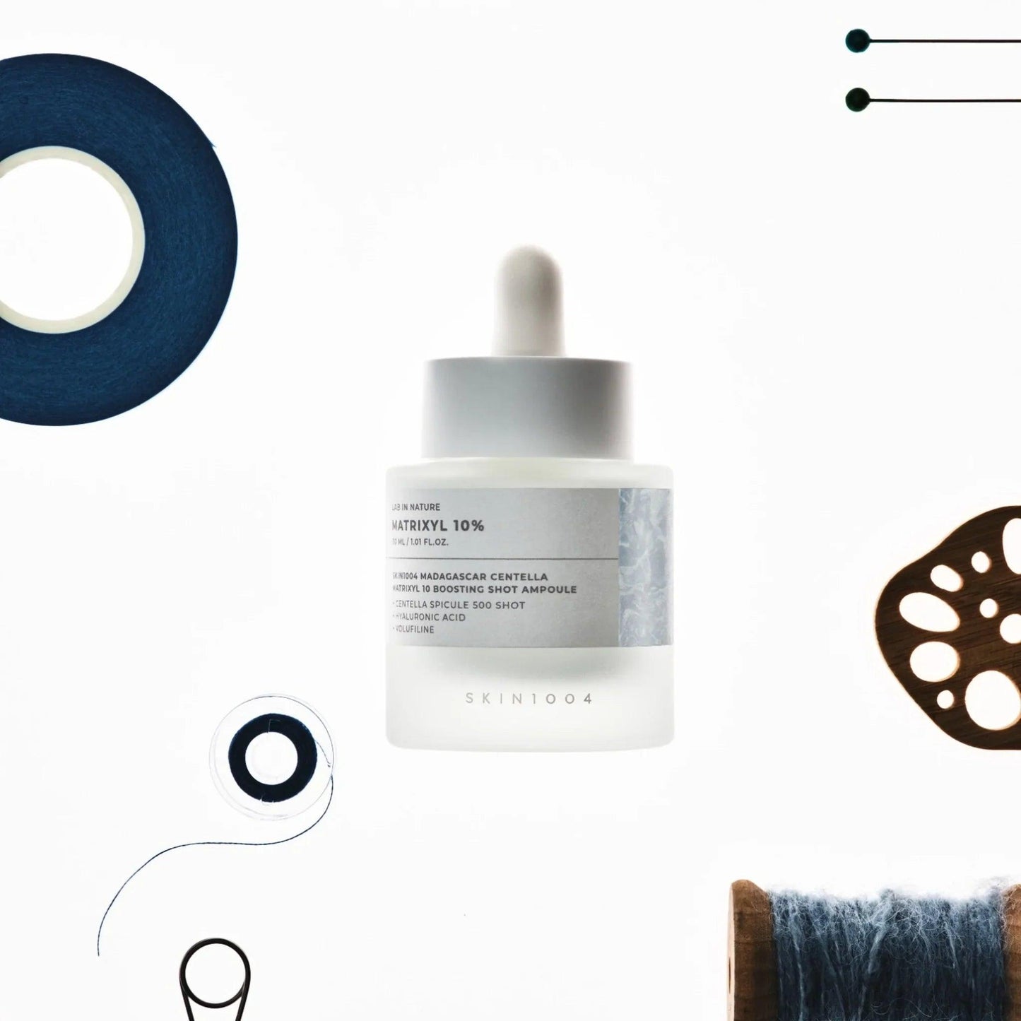Ampolla de suero Matrixyl 10% de Skin1004 sobre fondo blanco con accesorios de costura azul y marrón