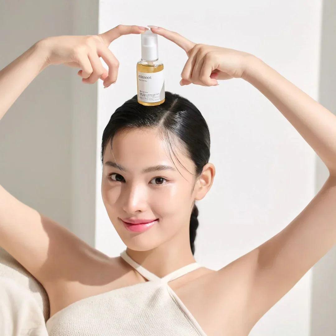Mujer sonriente con piel radiante sostiene serum Mixsoon sobre su cabeza, fondo blanco minimalista