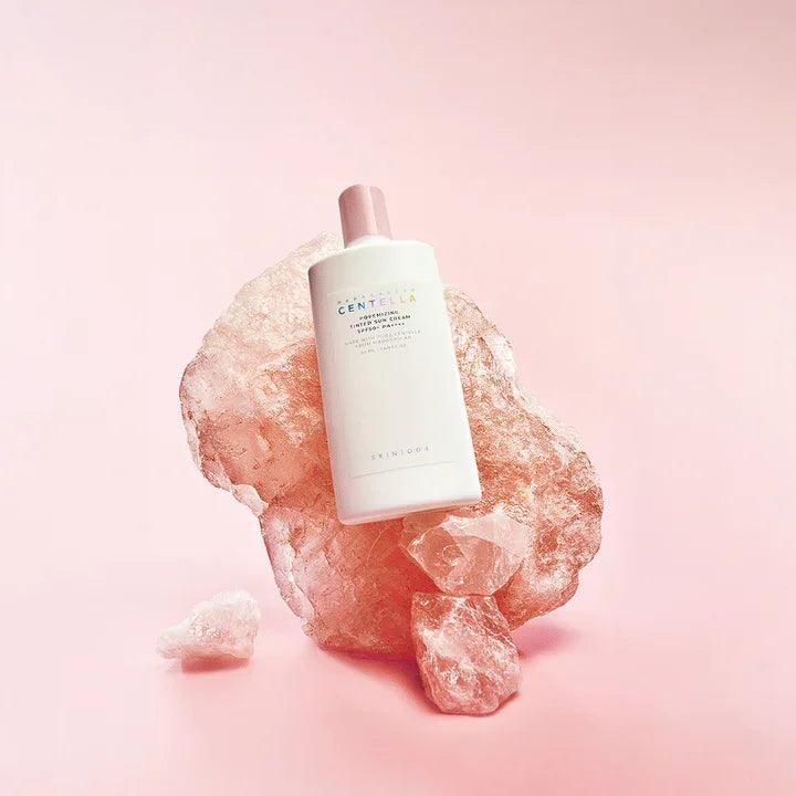 Botella de bloqueador solar Skin1004 Centella sobre cristales rosas con fondo rosa