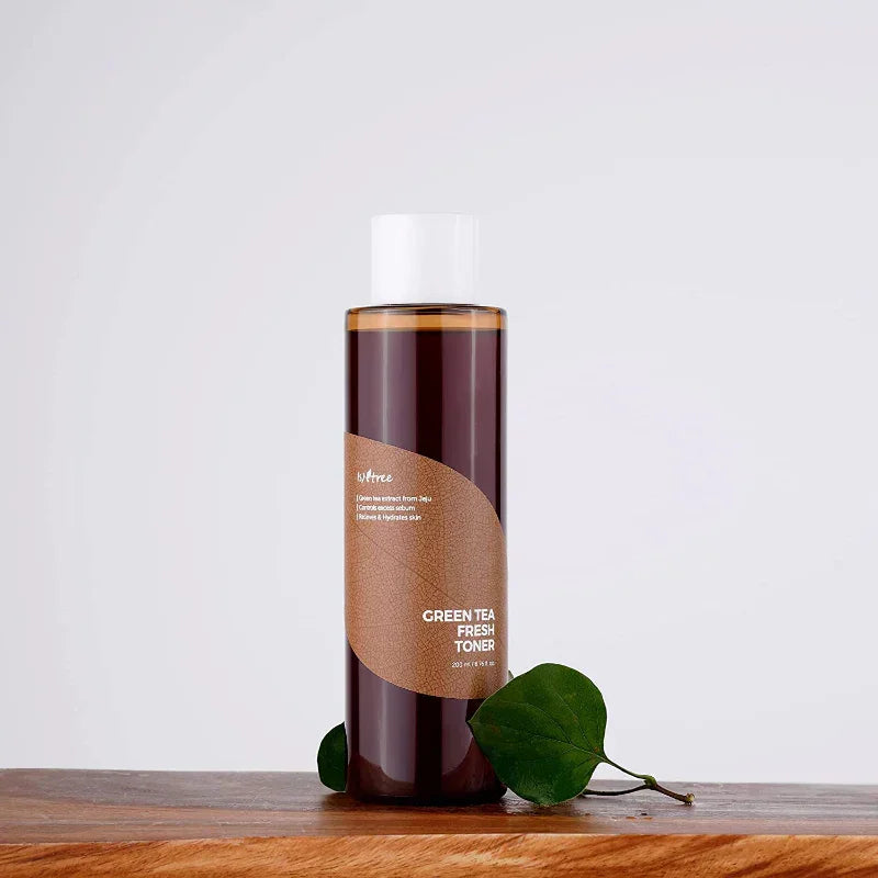 Botella de tónico facial Green Tea Fresh Toner sobre mesa de madera con hojas verdes