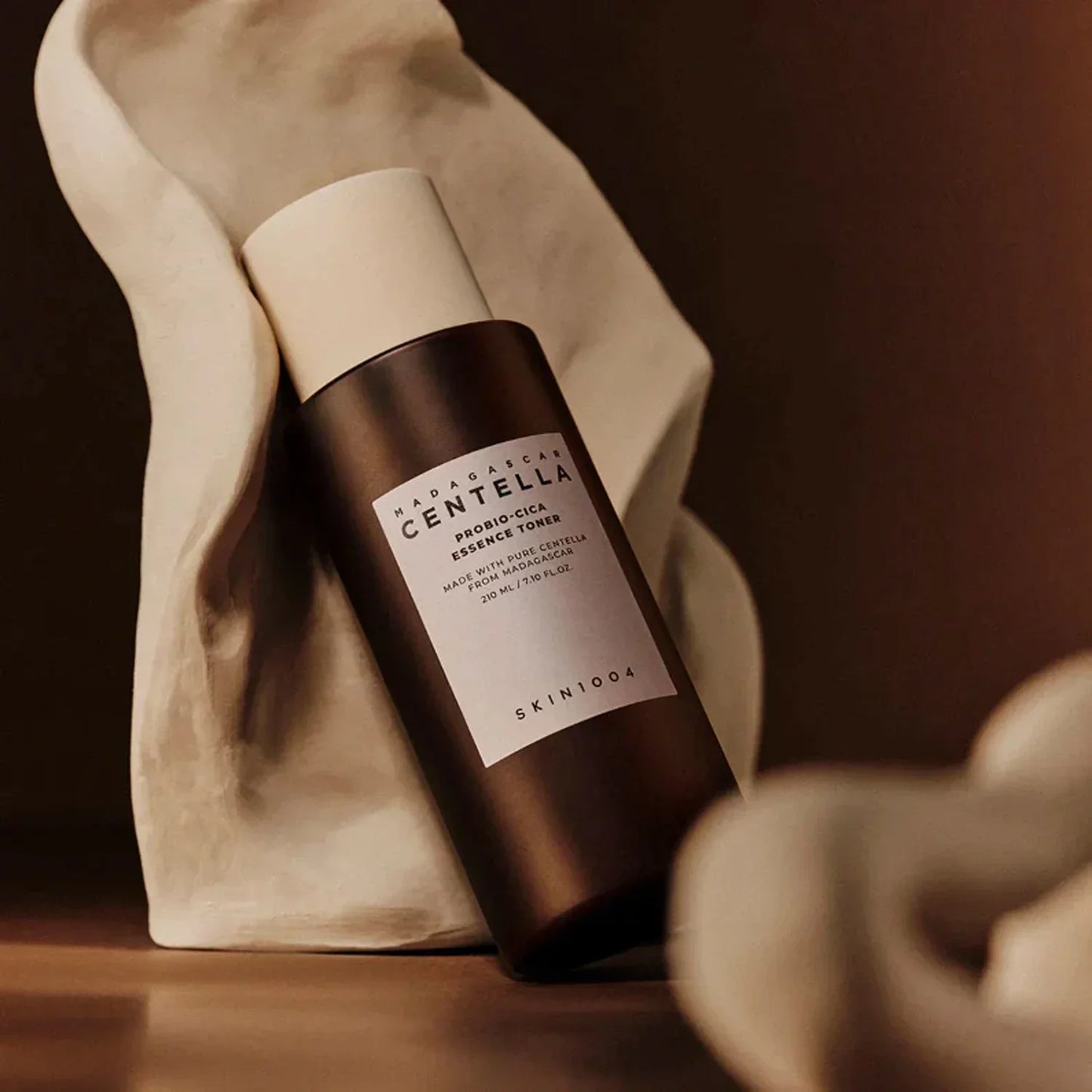 Tónico facial Madagascar Centella Probio-Cica essence en botella marrón sobre fondo beige y escultura