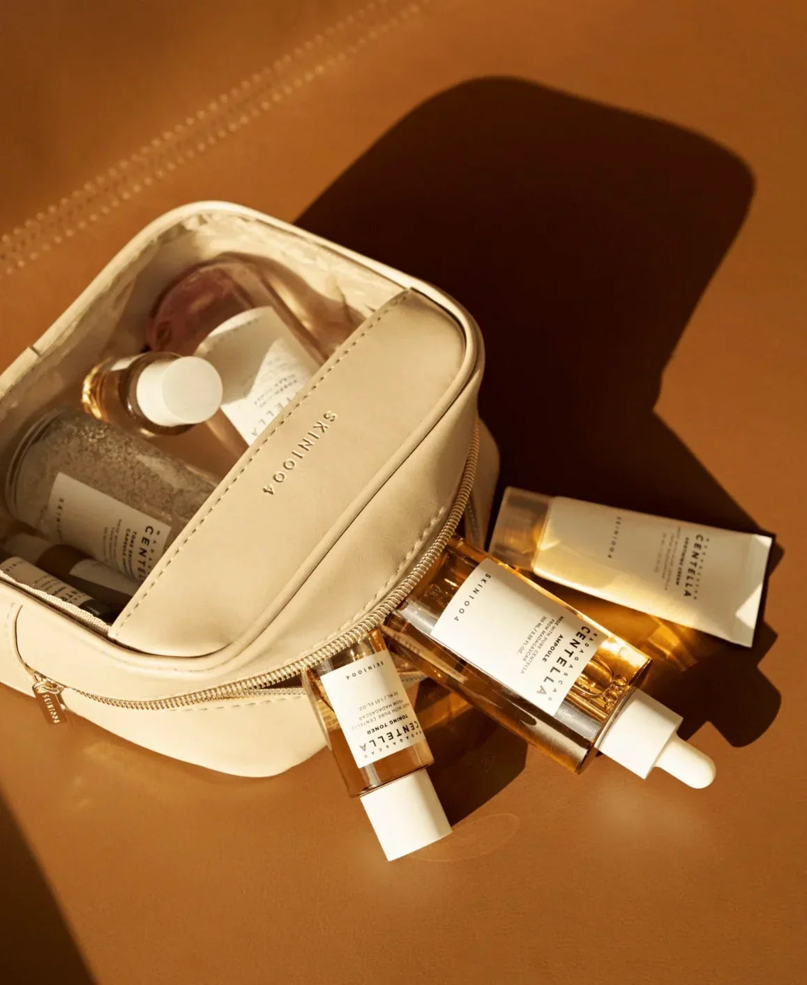 Neceser beige con productos de cuidado facial Centella de Skin1004 sobre superficie marrón