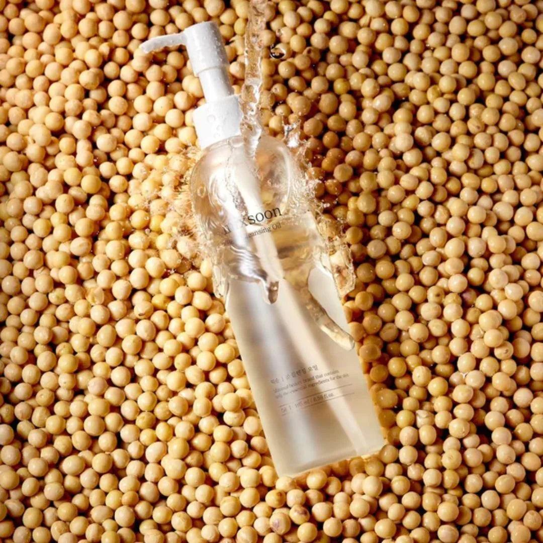 Botella transparente de aceite limpiador Mixsoon sobre granos de soja con salpicaduras de agua