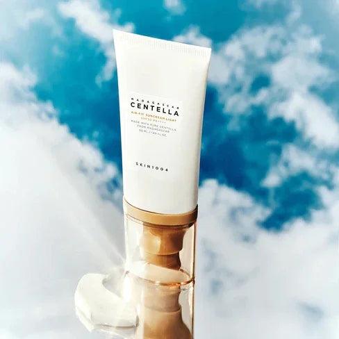 Protector solar Skin1004 Madagascar Centella SPF50 PA++++ en tubo blanco con fondo de cielo azul y nubes
