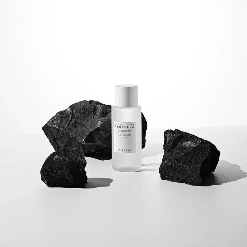 Tónico de Skincare Skin1004 Madagascar Centella con botella translúcida y rocas negras de fondo
