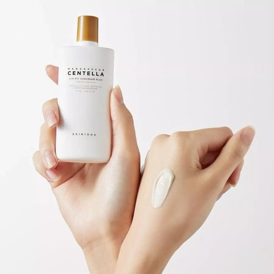 Manos sosteniendo protector solar Madagascar Centella Air-Fit con crema aplicada en la piel, fondo blanco